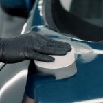 a gloved hand polishing the top of a blue car b