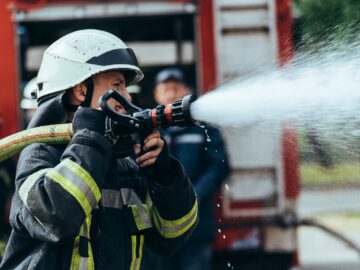 Image Source - photo dune selective focus of fire fighter with water hose extinguishing fire on street